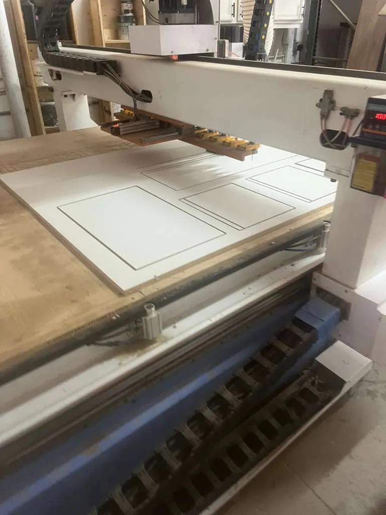 Router CNC con perfiles de puertas shaker cortados en un panel blanco